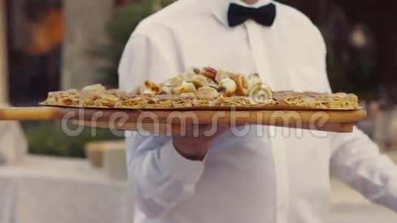 一位年轻的侍者在餐厅端酒慢吞吞地用一个大木盘端上美味的意大利菜视频的预览图