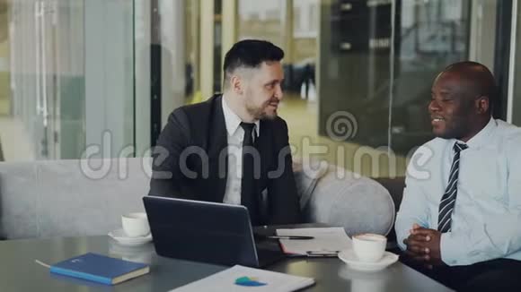 两个多民族商人看着笔记本电脑在玻璃咖啡馆笑商务学院玩得开心视频的预览图