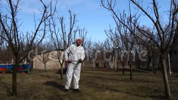 园丁穿着保护性的整体洒水在果园里用长喷雾器喷洒果树视频的预览图