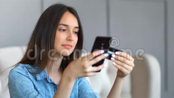 年轻漂亮的女士坐在家里客厅的沙发上用信用卡和智能手机上网购物视频的预览图