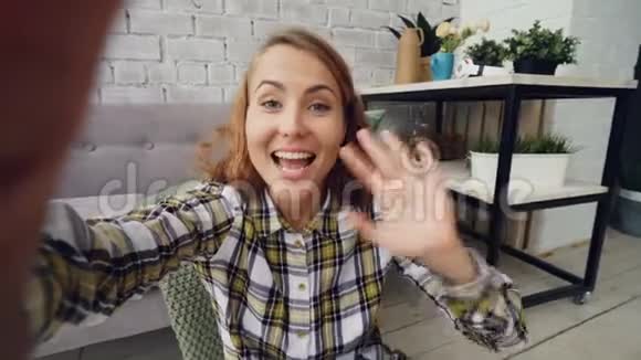 幸福的年轻女人看着相机拿着小玩意在网上和朋友聊天微笑和打手势的画像视频的预览图
