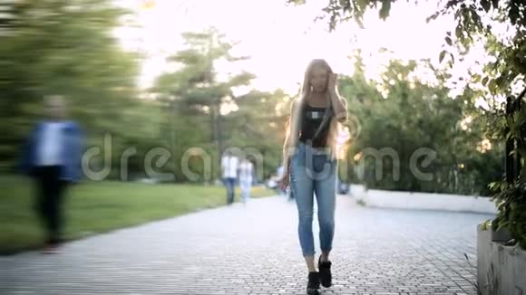 年轻的金发女郎飘逸的长发正走在公园里阳光下的背光正在闪耀视频的预览图