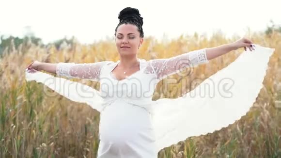 大自然背景下美丽的孕妇女孩拿着她的长花边连衣裙的边缘在风中飘扬夫人视频的预览图