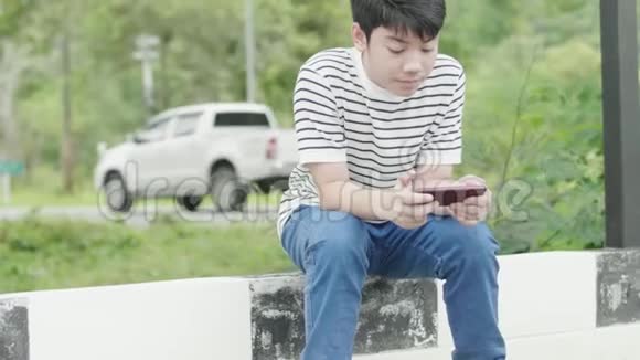亚洲十几岁的男孩在路边玩手机游戏视频的预览图