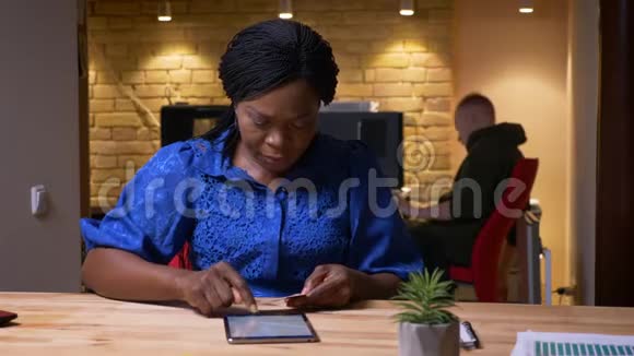 成年非裔美国女商人在办公室室内工作场所的平板电脑上发短信的特写镜头视频的预览图