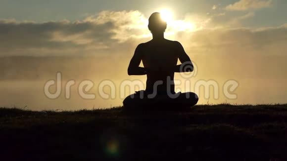 闪亮的人坐在湖岸上在日落时缓慢地祈祷和练习瑜伽视频的预览图