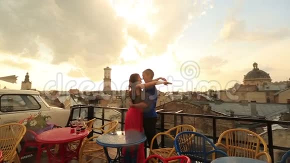 年轻的恋人在屋顶咖啡馆轻轻地亲吻在下雨的时候有着古城的景色浪漫的日落与天空视频的预览图