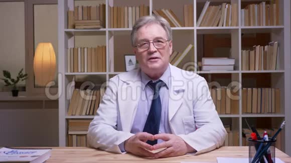 采访身穿白大褂的资深医生在书架背景上镜头交谈视频的预览图