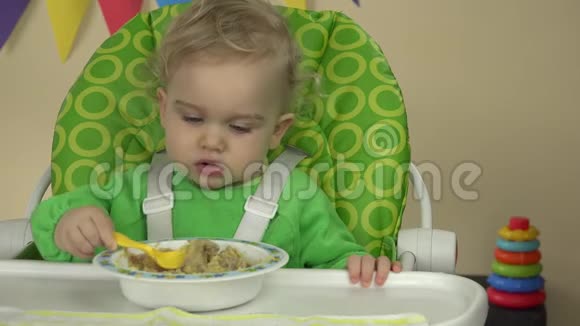 小女孩练习用勺子吃粥坐在婴儿椅上4K视频的预览图