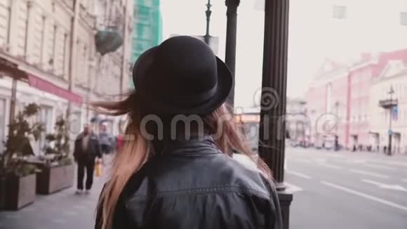 镜头跟随年轻的当地女孩穿着皮夹克和时髦的帽子沿着城市街道慢动作公共汽车在车站视频的预览图