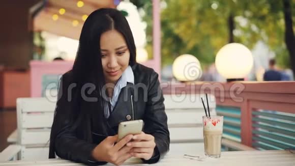 现代的亚洲女人正在使用智能手机在风和日丽的秋日在街头咖啡馆里给朋友发短信视频的预览图
