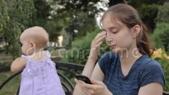 一个年轻的保姆看着智能手机屏幕拨开她的头发把智能手机放在一边移动一个女婴视频的预览图