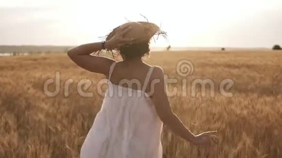 年轻女子一边拿着草帽一边跑在麦田里晴朗的天空中有太阳夏日罕见的观点视频的预览图