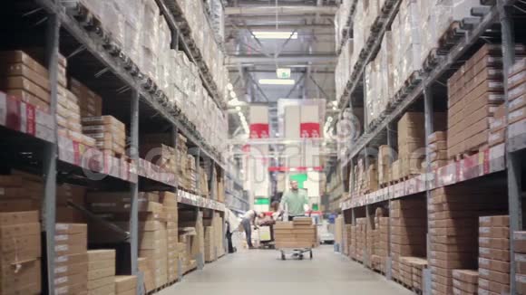 一个人正推着一辆装满箱子的手推车在仓库里的货架之间视频的预览图