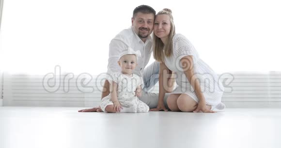 年轻迷人的夫妇和可爱的婴儿坐在白色的地板上看相机视频的预览图