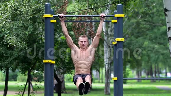 运动员在城市公园的水平杆上抬腿运动员在横杠上练习腹肌视频的预览图