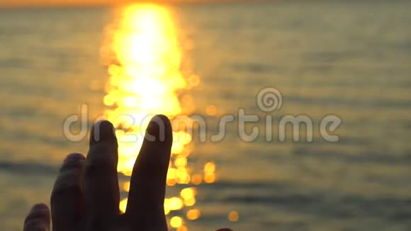 人手在海上日落海洋海滩一个人在大自然的背景海水上太阳和射线黄昏的光辉视频的预览图