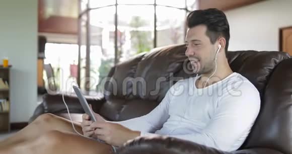 用平板电脑坐在客厅里的教练上打在线视频电话笑男人说网络视频的预览图