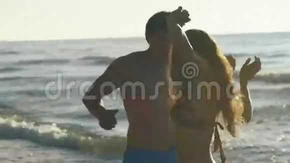 快乐的年轻夫妇在沙滩上玩冲浪英俊的男人和漂亮的女孩混在一起视频的预览图