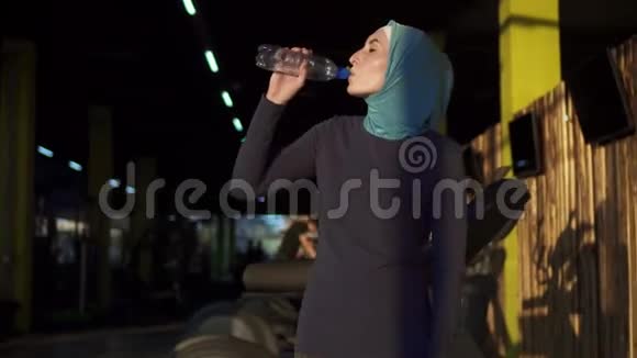 年轻的穆斯林女孩戴着头巾锻炼后从瓶子里喝水视频的预览图