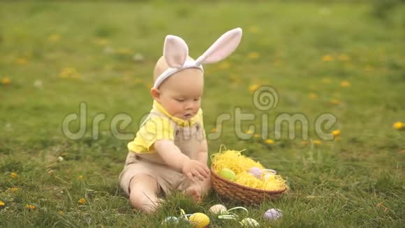 有趣的是一岁的婴儿正坐在公园的草地上扔复活节彩蛋复活节概念视频的预览图
