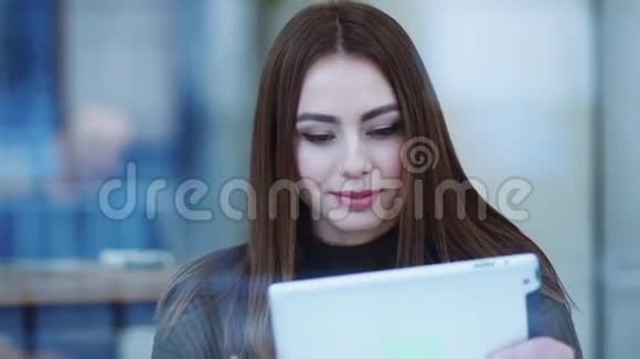 漂亮的年轻女人穿着时尚的毛衣坐在咖啡馆A喝咖啡使用平板电脑快乐地微笑快乐视频的预览图