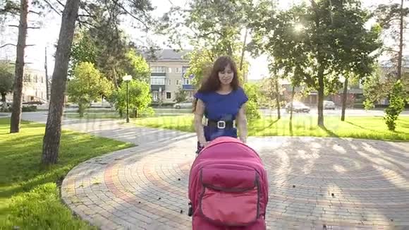 美丽的年轻妈妈带着婴儿车散步暑假在公园里休息一天视频的预览图