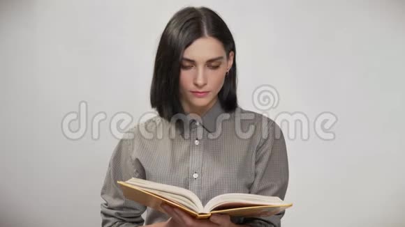 年轻漂亮的女人棕色短发拿着书看书然后看着相机微笑着白色的背景视频的预览图