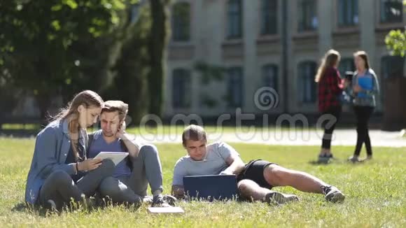大学生在草坪上使用笔记本电脑和平板电脑视频的预览图