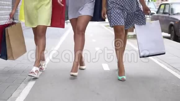 三个漂亮的女朋友购物后带着包裹沿着街走互相交谈慢动作视频的预览图