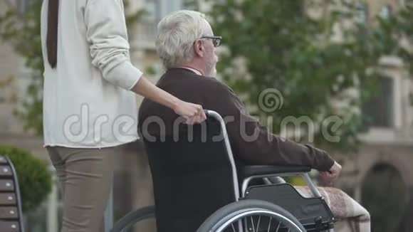 年轻女性与残疾老年男性轮椅同行家庭支持视频的预览图