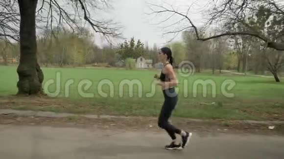 年轻健康的女孩夏天在公园里带着耳机跑步健康的生活方式运动观念侧视视频的预览图