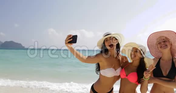 沙滩上的女孩在手机上拍照比基尼的快乐女人在夏日度假时脱掉草帽视频的预览图