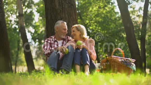 快乐健康的老夫妇在草地上放松拿着苹果拥抱野餐视频的预览图