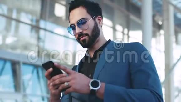 一个留胡子的成功男人在机场入口处用手机旋转滑动屏幕环顾四周视频的预览图