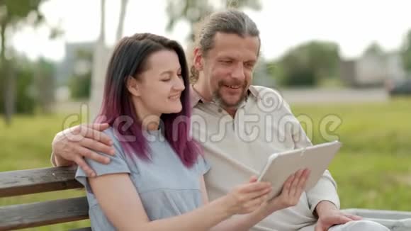 放松迷人的中年男子留着长长的灰色头发一个年轻的女人染着头发拥抱着看着一张照片视频的预览图