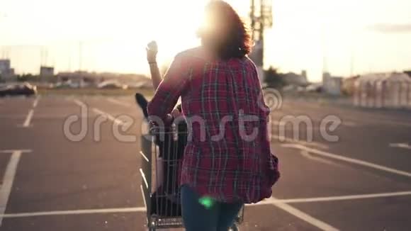 一个年轻的女人推着购物车而她的朋友在日落时坐在里面镜头耀斑视频的预览图