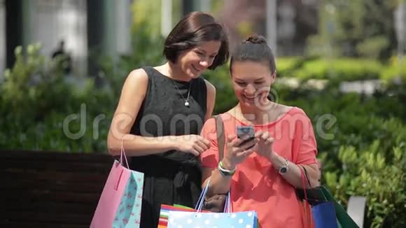两个时尚女孩带着袋子在街上用智能手机购物美女用电话视频的预览图