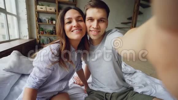 一对情侣在家里坐在床上一起自拍摆姿势接吻和玩的镜头视频的预览图