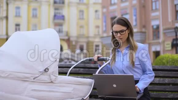 多任务妈妈摆动婴儿车和工作笔记本电脑坐在长凳上视频的预览图