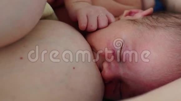 妈妈正在和刚出生的新生儿躺在一起用一只抱着她小手的乳房喂养他视频的预览图