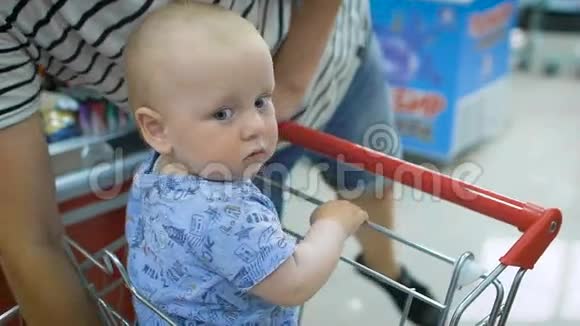 一个小婴儿坐在超市的购物车里而他的父亲则在结账处付钱买东西视频的预览图
