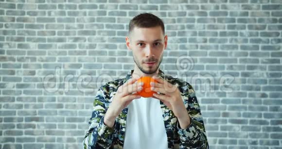 快乐的人抱着橘子眼睛躲在砖墙背景下的水果后面视频的预览图
