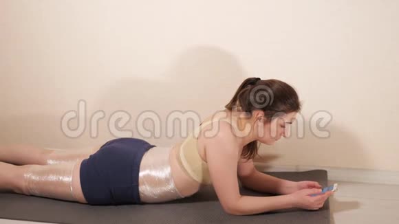 女人躺在健身房的垫子上拿着电话视频的预览图