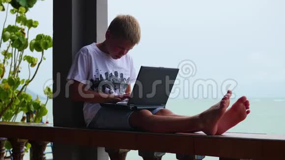 年轻人在笔记本电脑上玩坐在露台上靠近大海和海滩视频的预览图