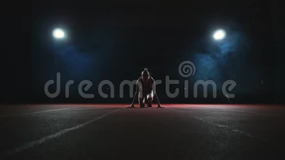 瘦小的女运动员可以在跑道上的垫子上慢慢地在烟雾中奔跑视频的预览图