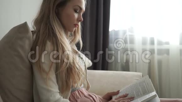 美丽的年轻女子坐在沙发上看书微笑着视频的预览图