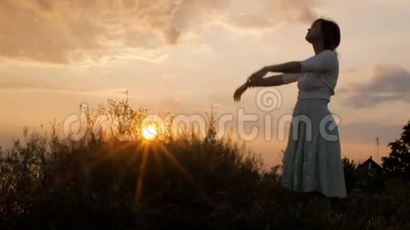 日落时分一个快乐的女孩在田野里的剪影年轻的女人在大自然中行走休闲和保健的概念视频的预览图