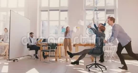 慢动作快乐女员工骑椅子沿着现代办公室有趣的商务人士一起庆祝成就视频的预览图