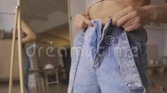 美丽的年轻运动女人看着她的腹肌漂亮的年轻运动女孩穿着牛仔裤看着她的腹肌视频的预览图